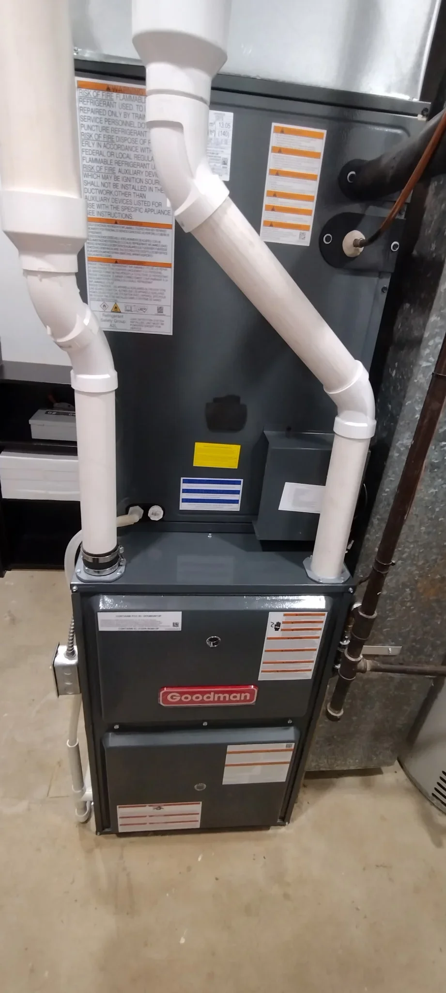 Newly installed Goodman furnace with white PVC venting and labeled safety documentation